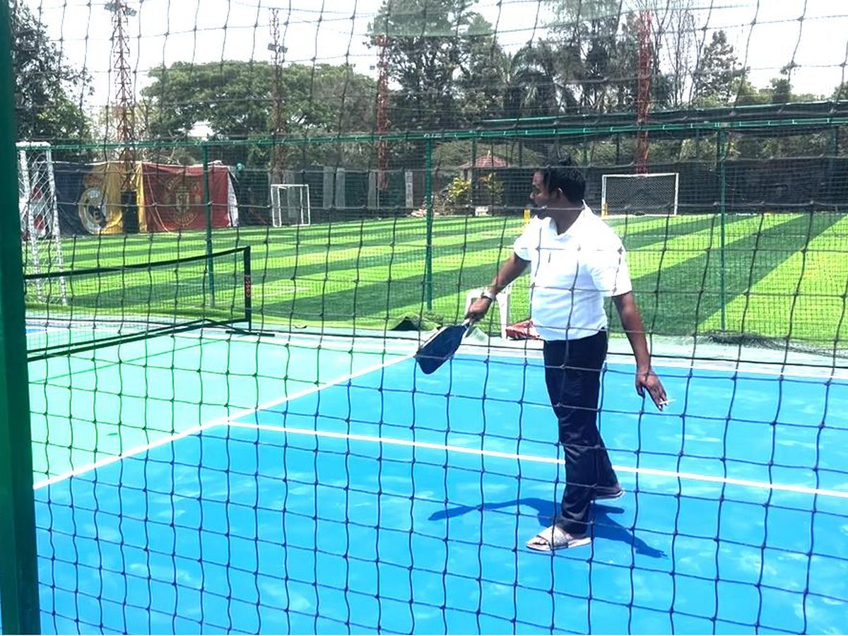 Blue acrylic multi-sport court enclosed in netting beside a green turf football ground